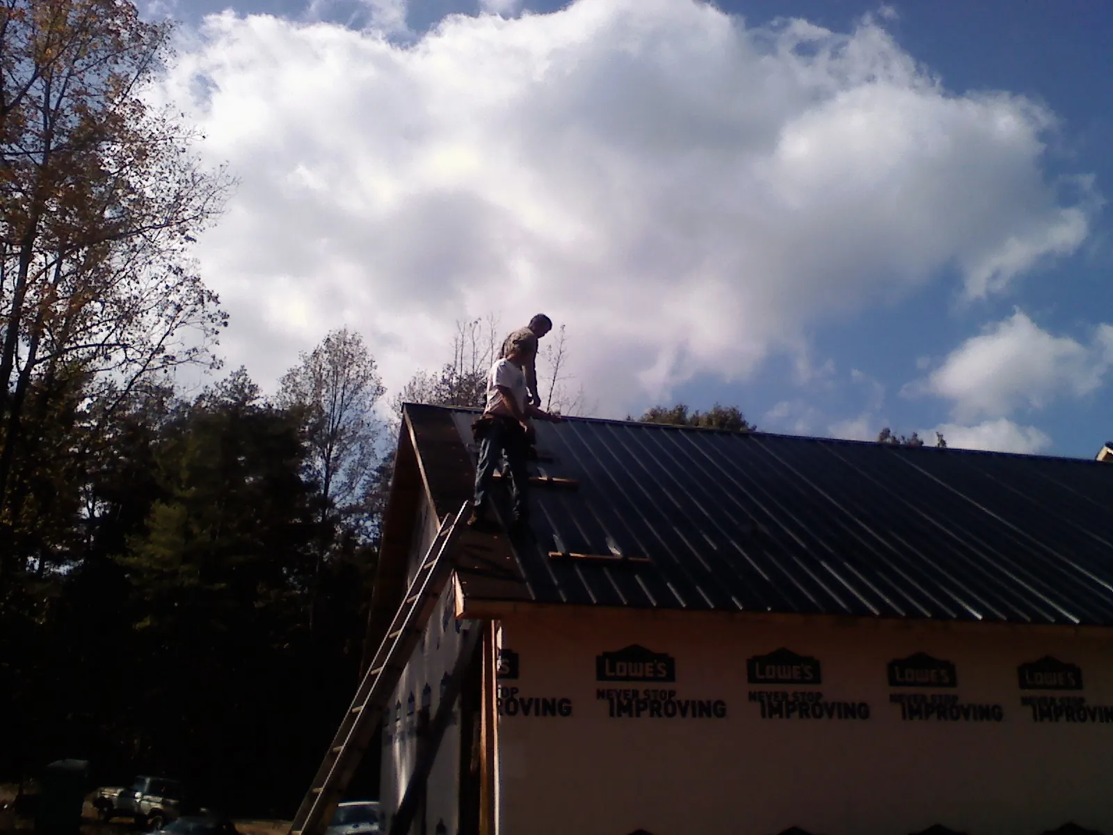 Roofer fastening dark metal panels high against a cloudy sky, from a Roof Inspection job in Maxwell