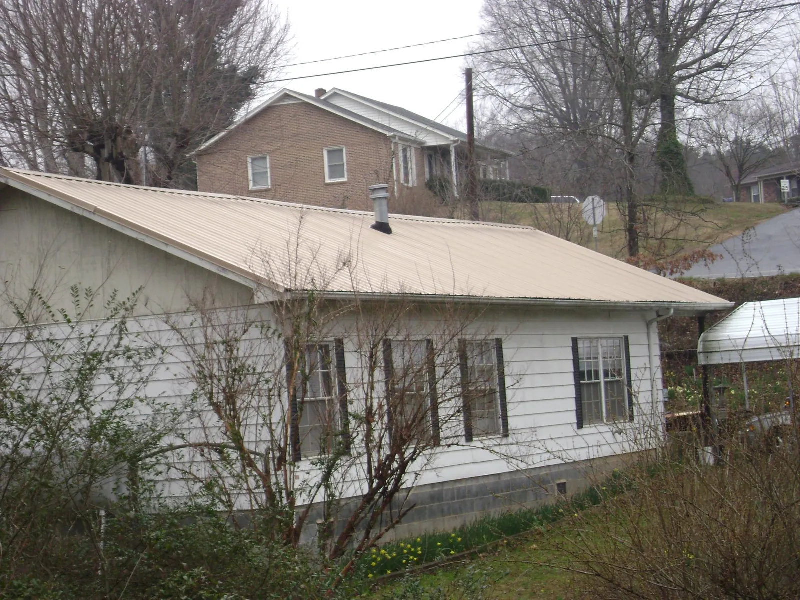 Tan metal roof on a white sided house set into a hillside — Commercial Roofing by Roofing Brothers in Maxwell